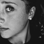 Home Captivating black and white portrait of a woman with freckles and pearl earrings.